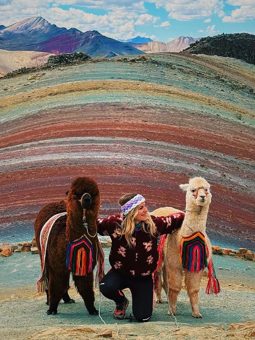 Alpacas beside a traveller in front of Palcoyo’s rainbow mountains
