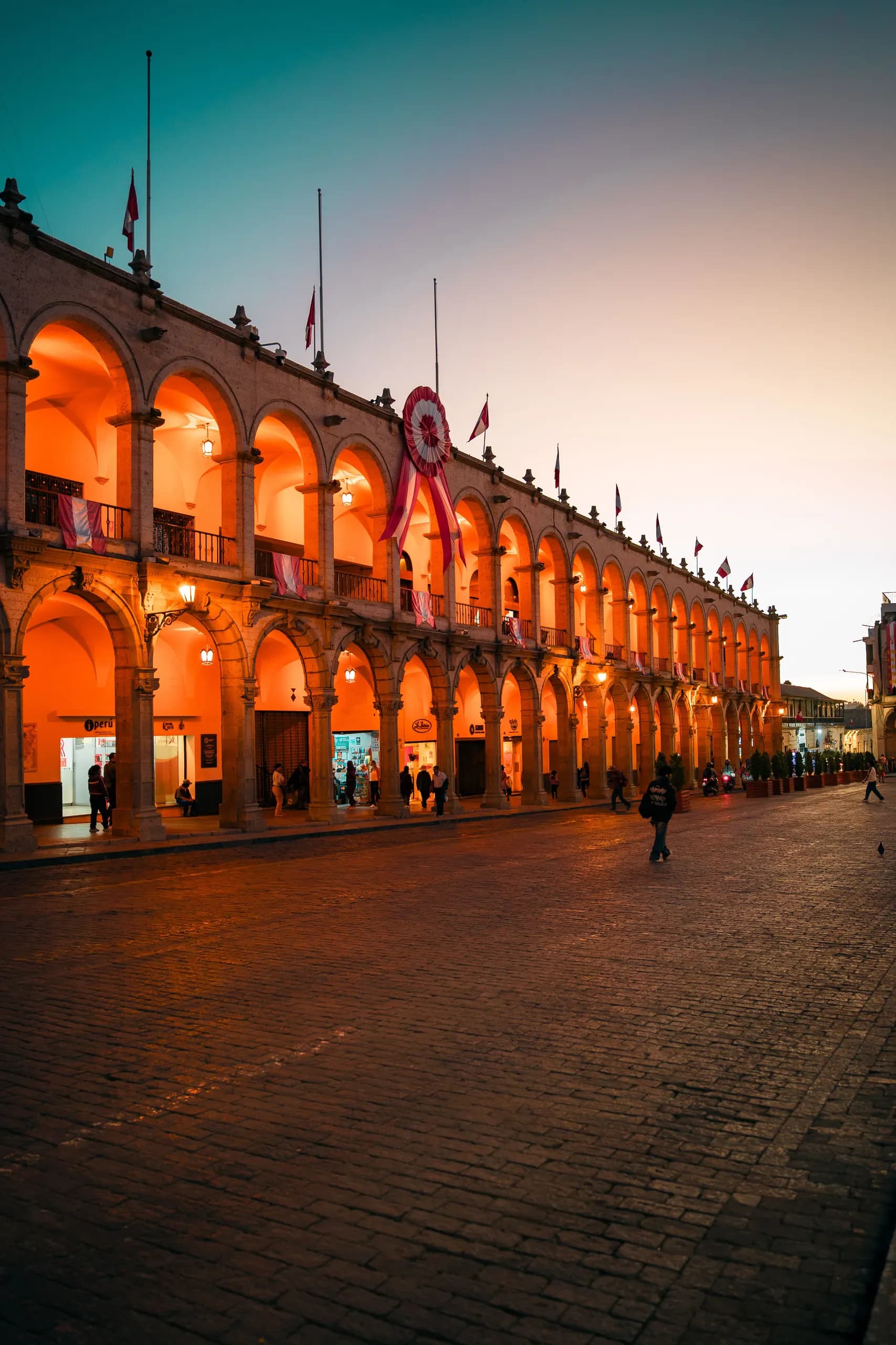 Illuminated arcades beside a square at dusk