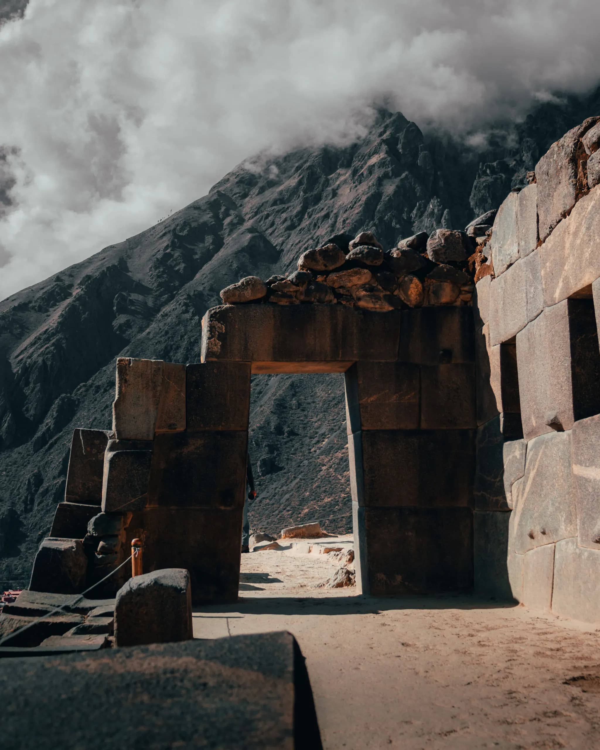 Inca trapezoidal stone doorway beside a cloud-covered mountainside