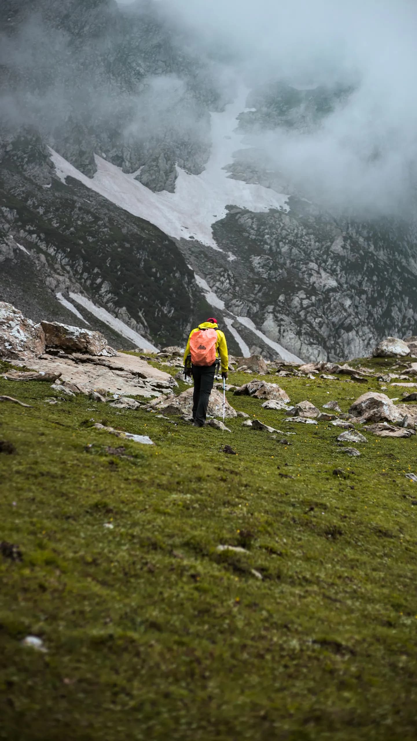 Hiker following a trail between rocky slopes and cloud-covered mountains