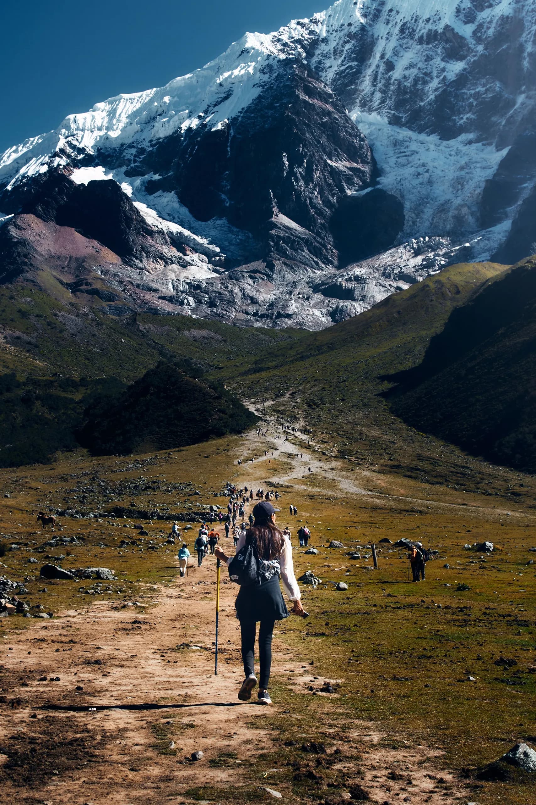 Hiker on a trail below a snowy peak