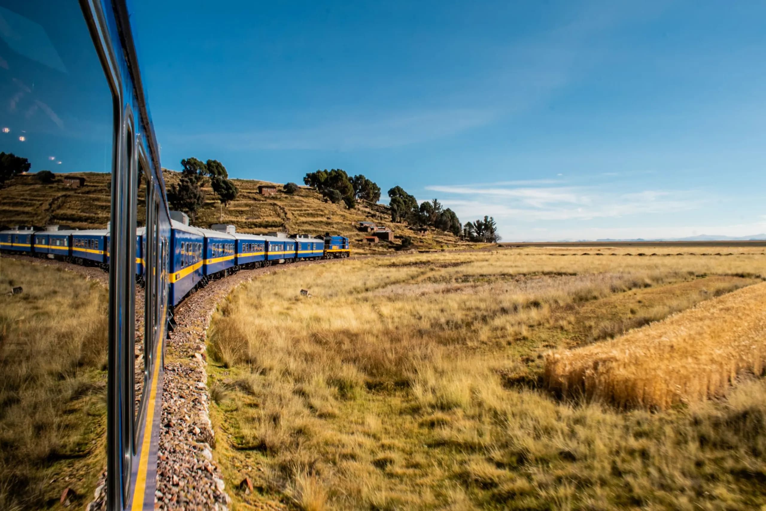 A passenger train crossing a plain of golden grass beneath a blue sky