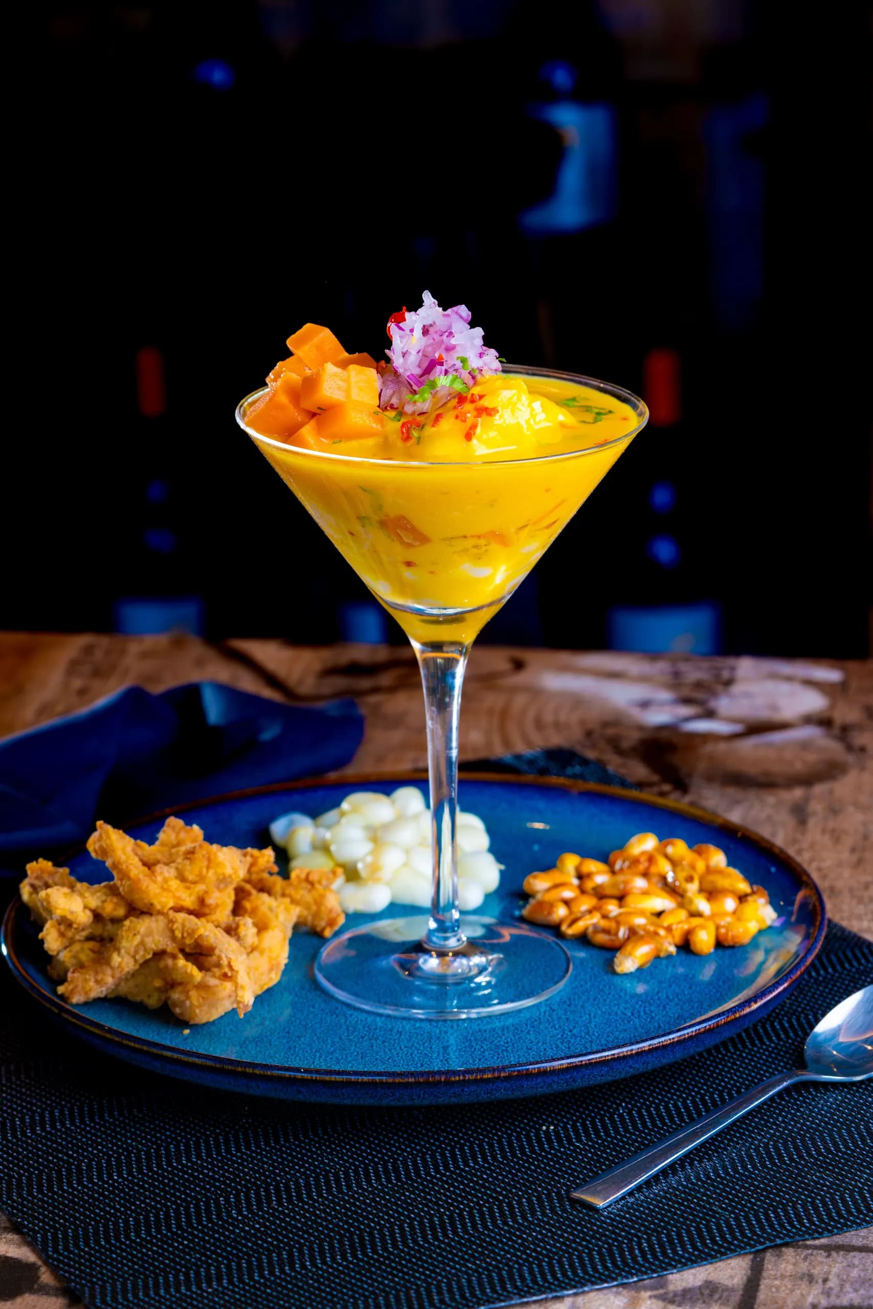 © nano erdozain · Pexels Ceviche served in a glass with yellow sauce and red onion, accompanied by corn on a blue plate