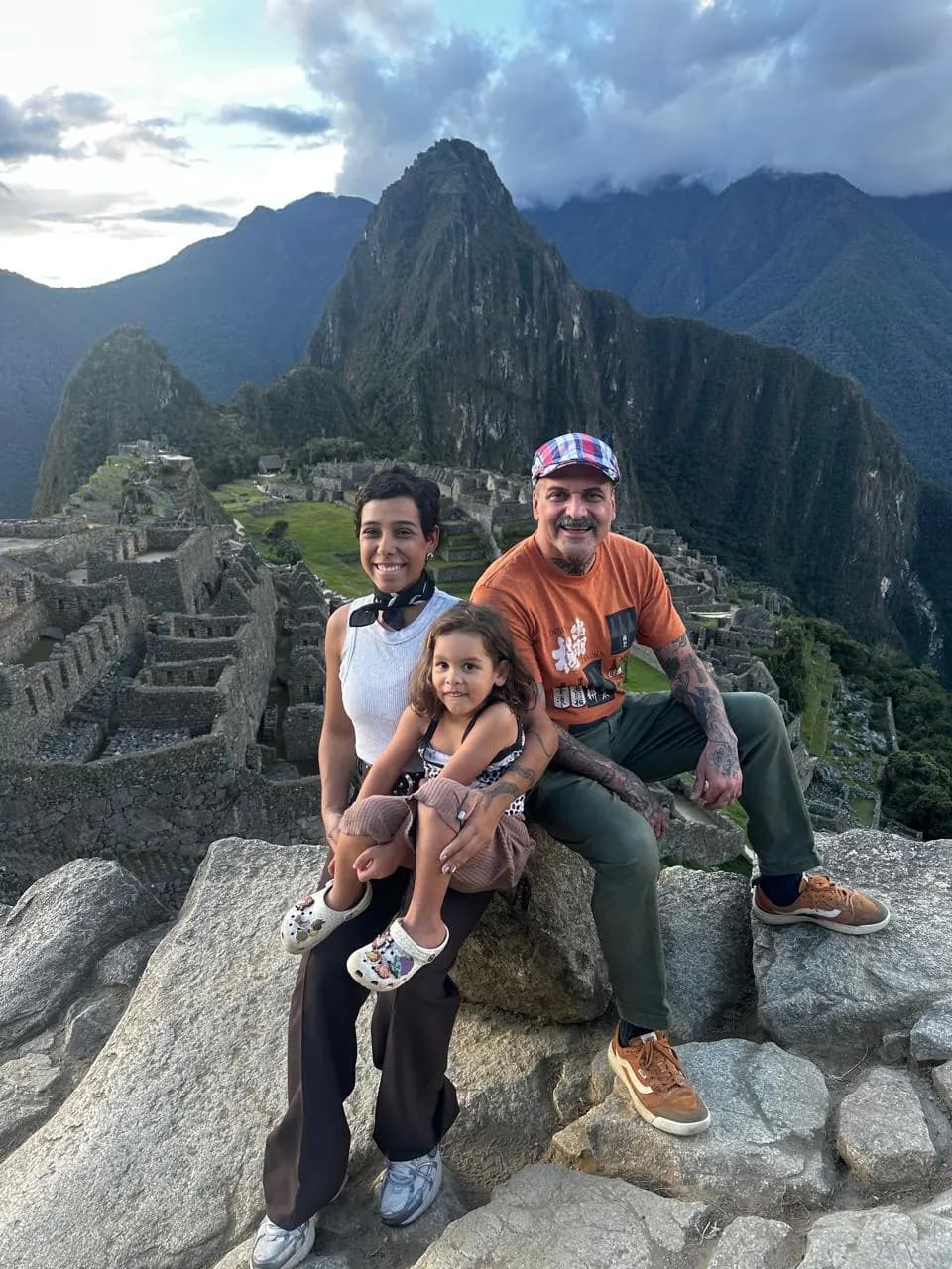 © Vacations in Peru Family seated on a stone wall at Machu Picchu, with the ruins and Huayna Picchu in the background