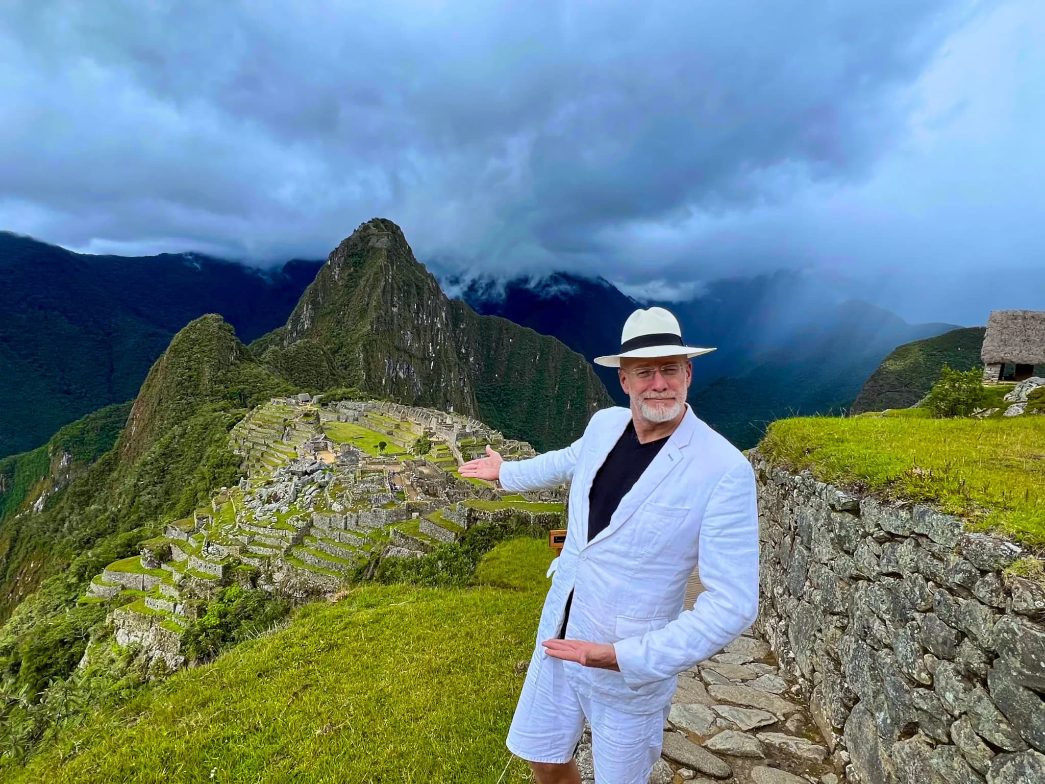 © Vacations in Peru Traveller wearing a hat and white clothing beside the ruins of Machu Picchu, with Huayna Picchu beneath the clouds